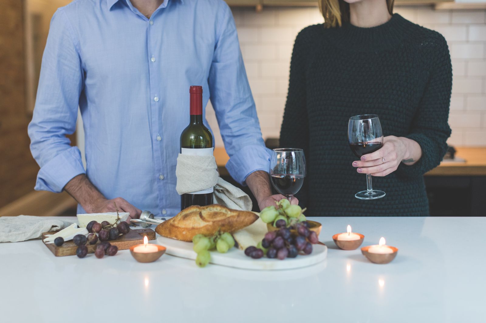 Vin rouge, pain, raisins et fromages sur un plan de travail éclairé aux bougies